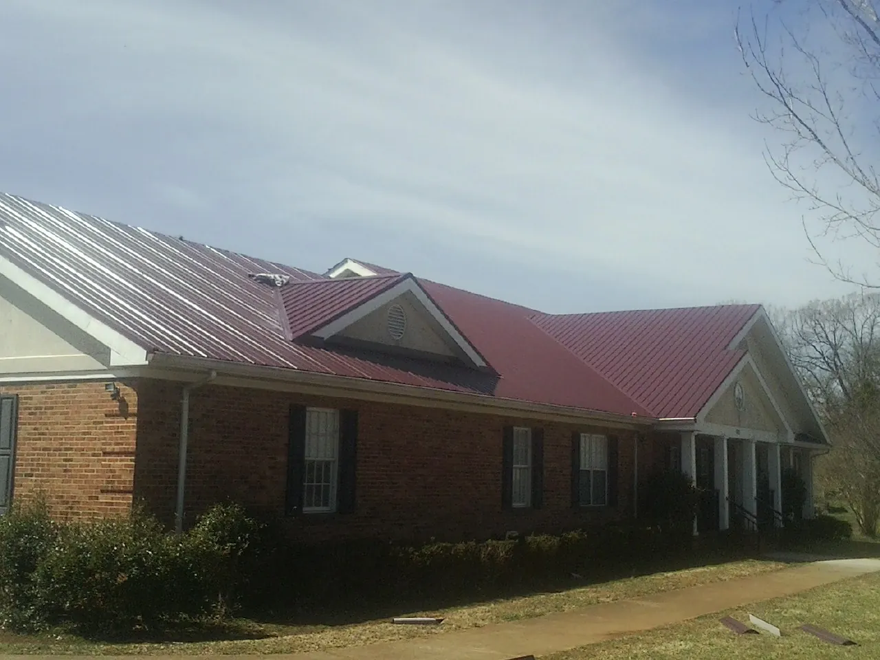Red metal roof with gabled entries on a long brick building, from a Hail Damage Roof Repair job in Adamsville