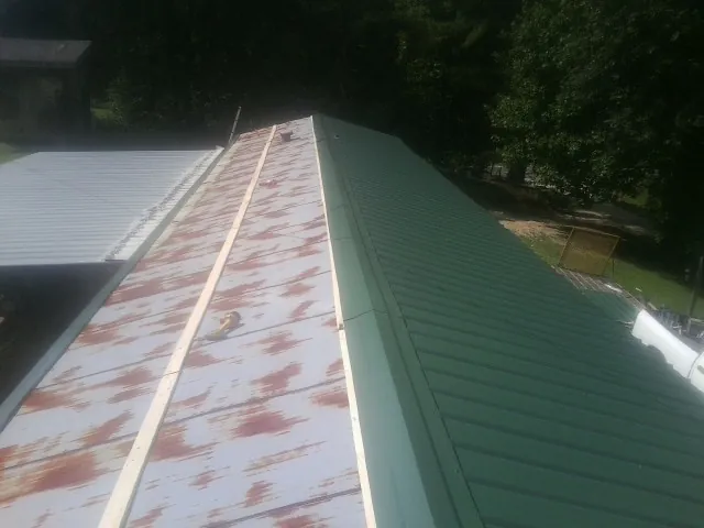 Old rusted panels beside newly installed green metal roofing — Wind Damage Roof Repair by Roofing Brothers in Adamsville